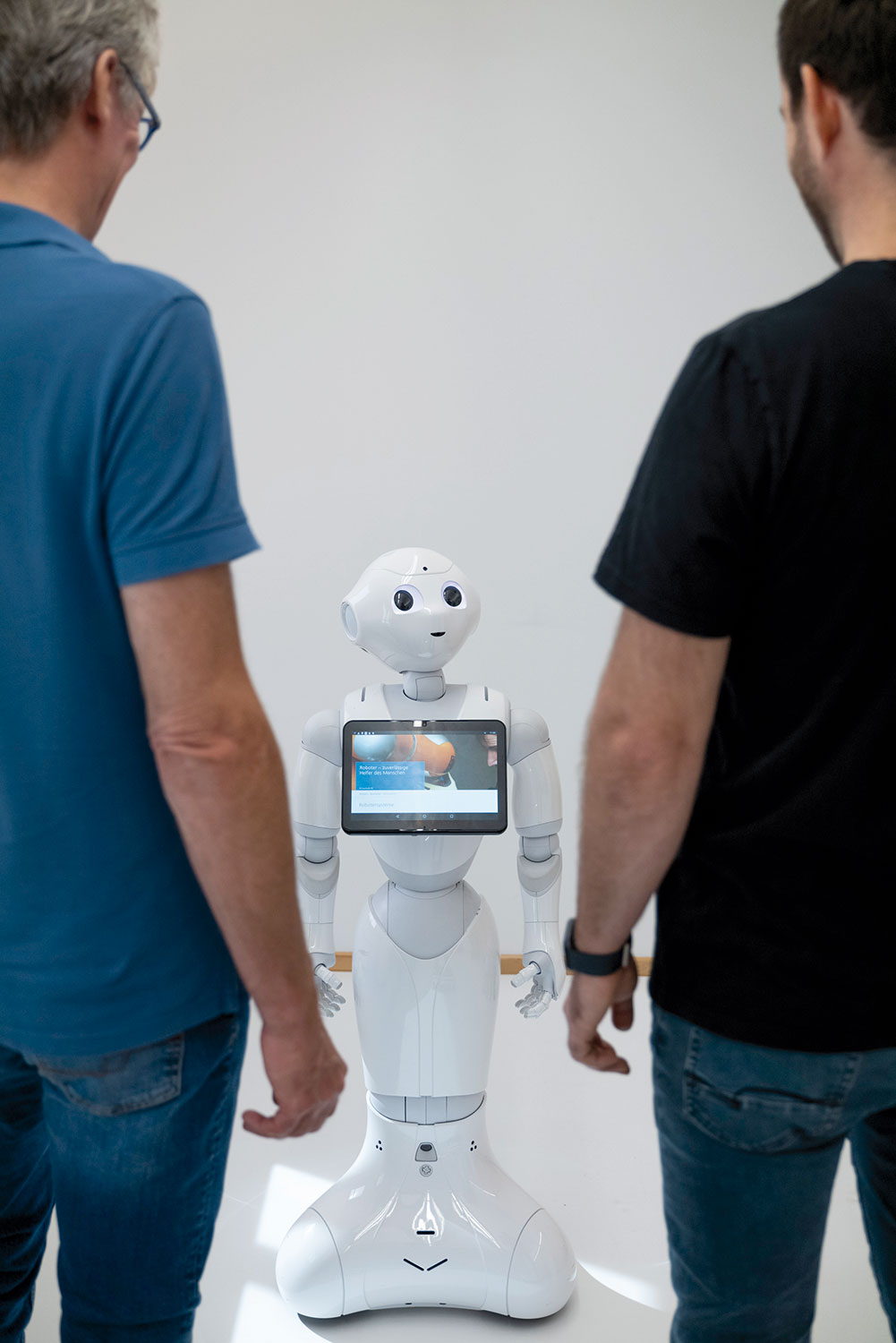 Zwei Forscher stehen mit dem Rücken zur Kamera und blicken auf den Service-Roboter Care-o-Bot, der in Blickkontakt mit einem der beiden ist.