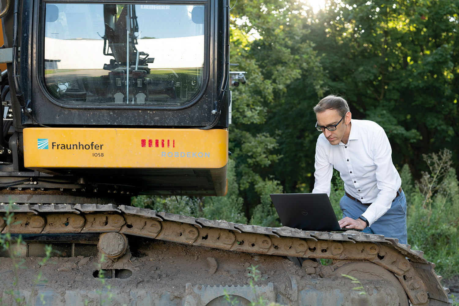 Der Forscher Janko Petereit steht im Freigelände neben einem Raupenbagger, gebeugt über einen Laptop, der auf dem Raupenlaufwerk liegt. 