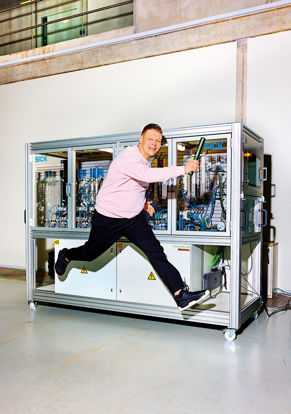 Fraunhofer IPA-Wissenschaftler Daniel Umgelter beim inszenierten Staffellauf mit einem Staffelstab in der Hand vor einem Schaukasten mit Sensortechnologie.