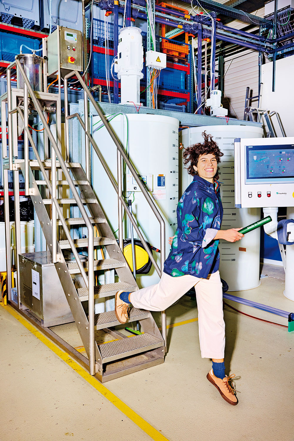 Fraunhofer IGCV-Wissenschaftlerin Violetta Schumm, im inszenierten Stapellauf mit einem Staffelstab in der Hand, auf dem Sprung von der Treppe einer Nassvliesanlage.