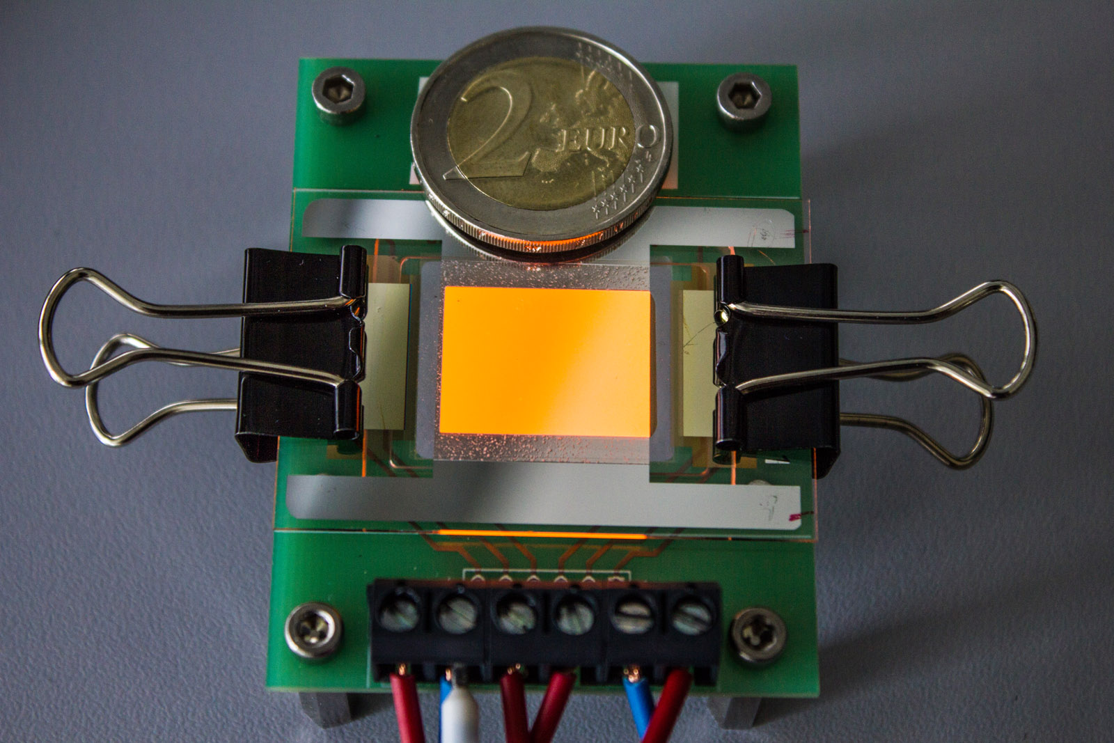 Orange leuchtende OLED auf einer Graphen-Elektrode. Die Zwei-Euro-Münze dient als Größenvergleich. 