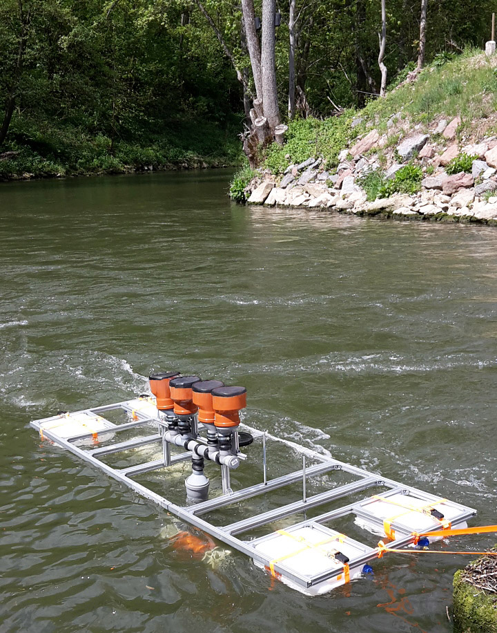 Feldversuch mit DEGREEN-Generatoren in einem Fließgewässer. Die Anregung der Silikonmembranen erfolgt über den Unterdruck in den wasserdurchströmten Venturi-Rohren unter dem Floß.