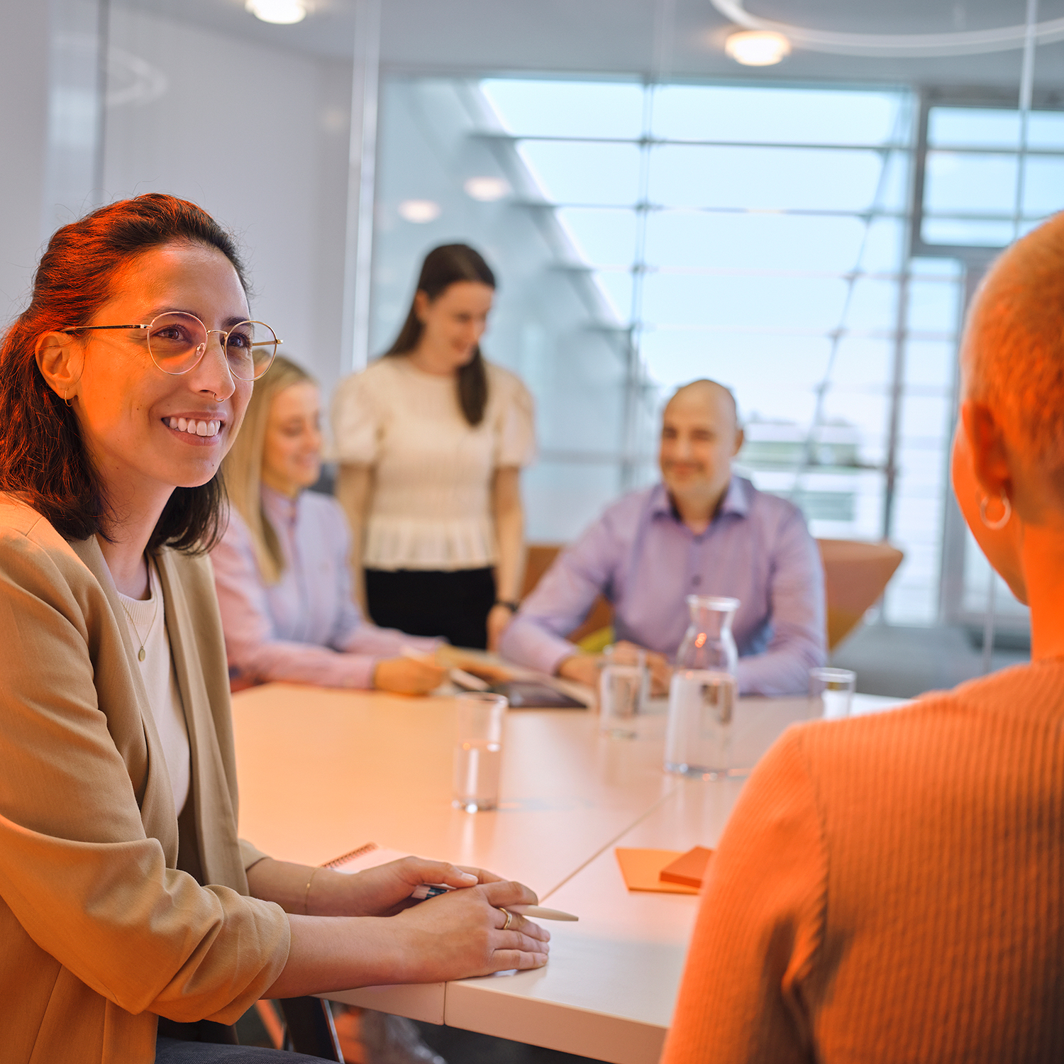 A woman sits at a table talking to another person. Three other people are sitting in the background.