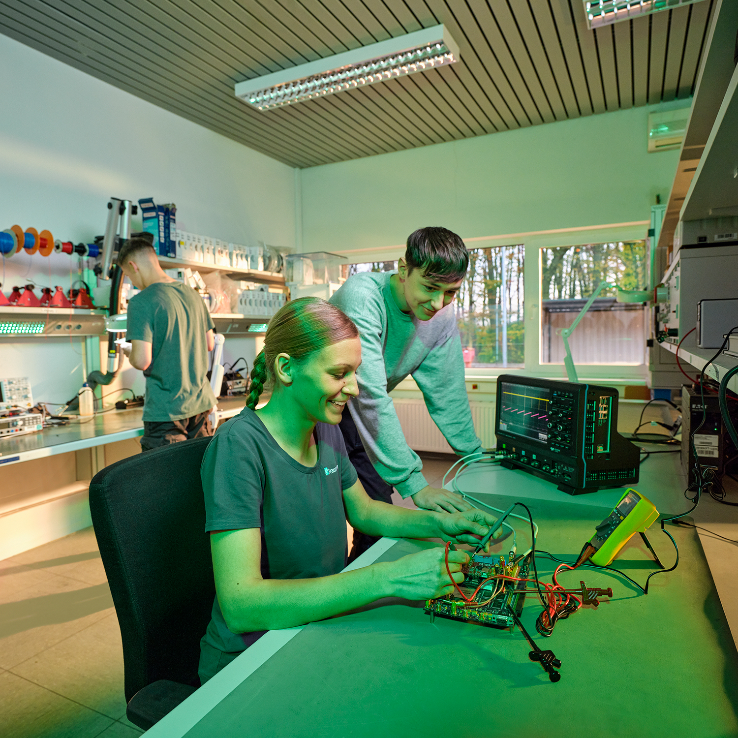 A young woman and a young man are sitting at a workbench soldering. 