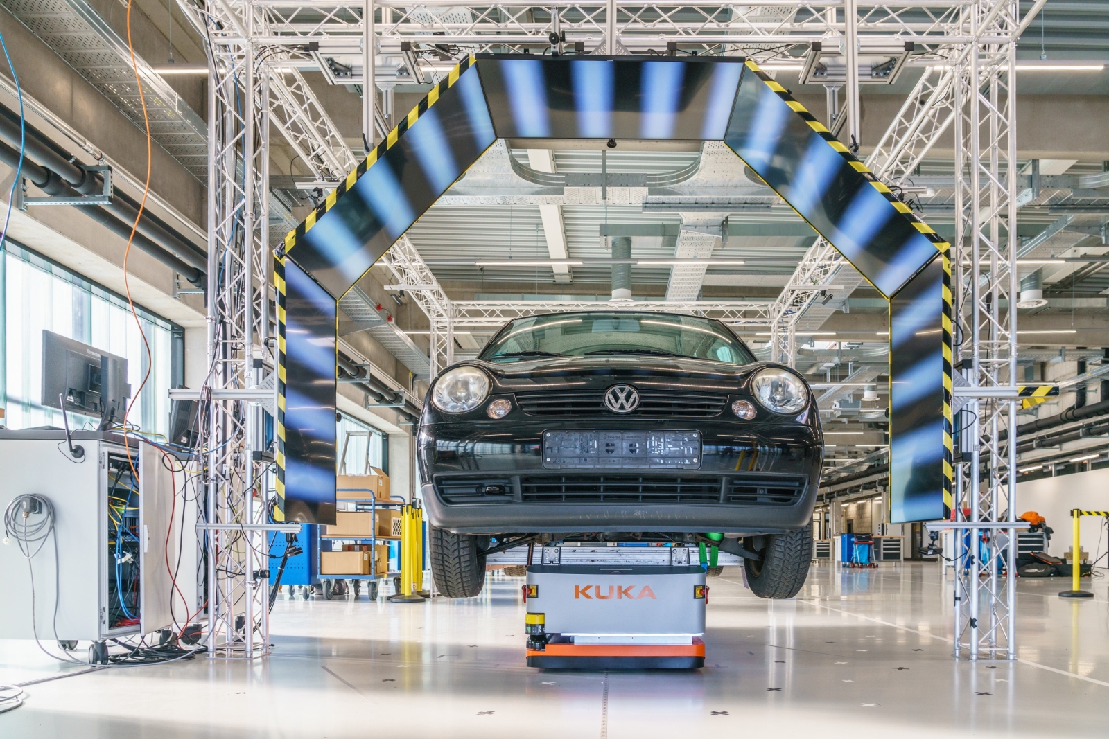 In the AutoInspect demonstrator, the car body is transported to the inspection stations on a conveyor system. The picture shows the deflectometry portal: The software can detect surface defects based on the reflection of the striped patterns displayed on the monitors.