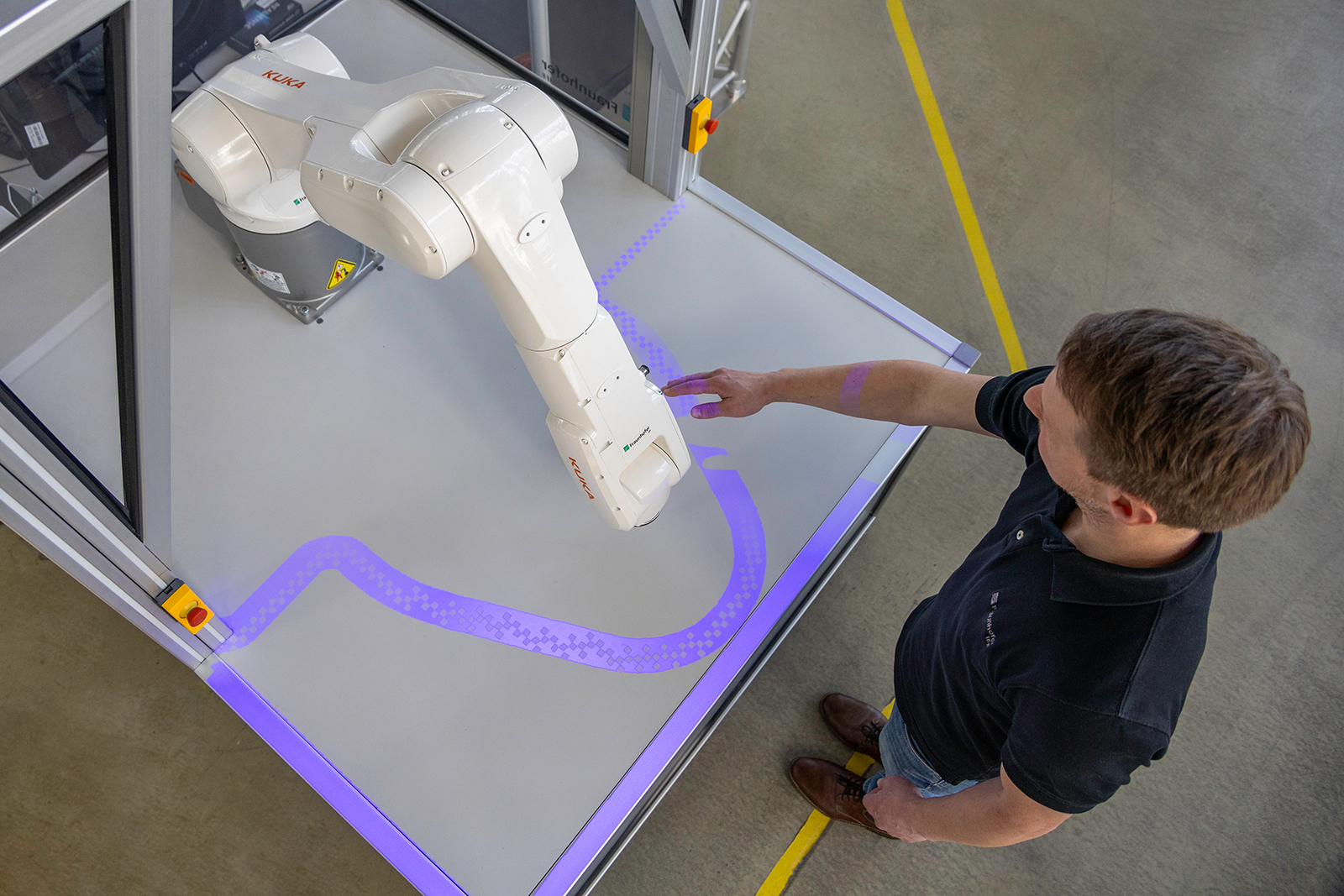 Die patentierte PARU-Sicherheitstechnologie erzeugt sichtbare Lichtvorhänge um den Arbeitsraum des Roboters. Die blau beleuchteten Sicherheitslinien passen sich dynamisch an die Bewegungen der Maschine an und ermöglichen eine sichere Interaktion zwischen Mensch und KI-gesteuerten Robotern.