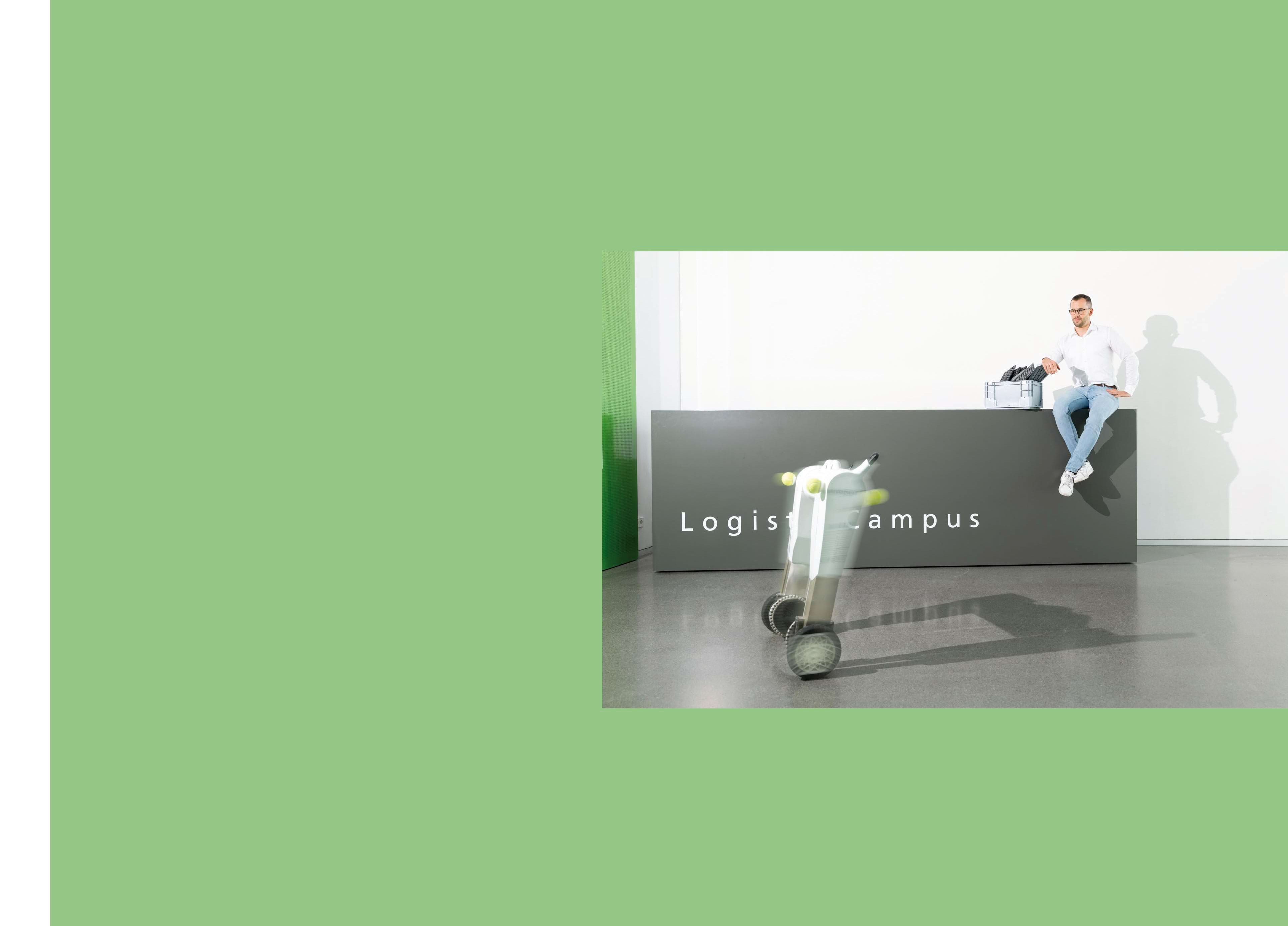 Der Elektronik-Ingenieur Leon Siebel-Achenbach, auf dem Empfangstresen des Logistik Campus sitzend, vor ihm rollt der Serviceroboter evoBOT auf zwei Rädern durch den Raum.